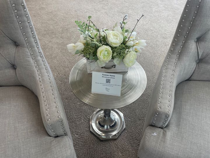 A small table with white flowers between 2 chairs on the left and right of it.